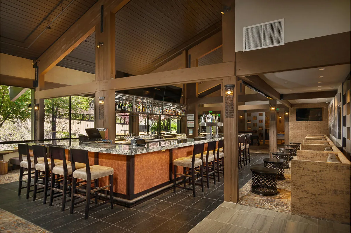 The image captures the bar area within CURRENTS, featuring a sleek counter, comfortable seating, and an inviting bottle display. The mood is lively yet intimate, with warm lighting that encourages social gatherings and relaxed conversations over drinks.