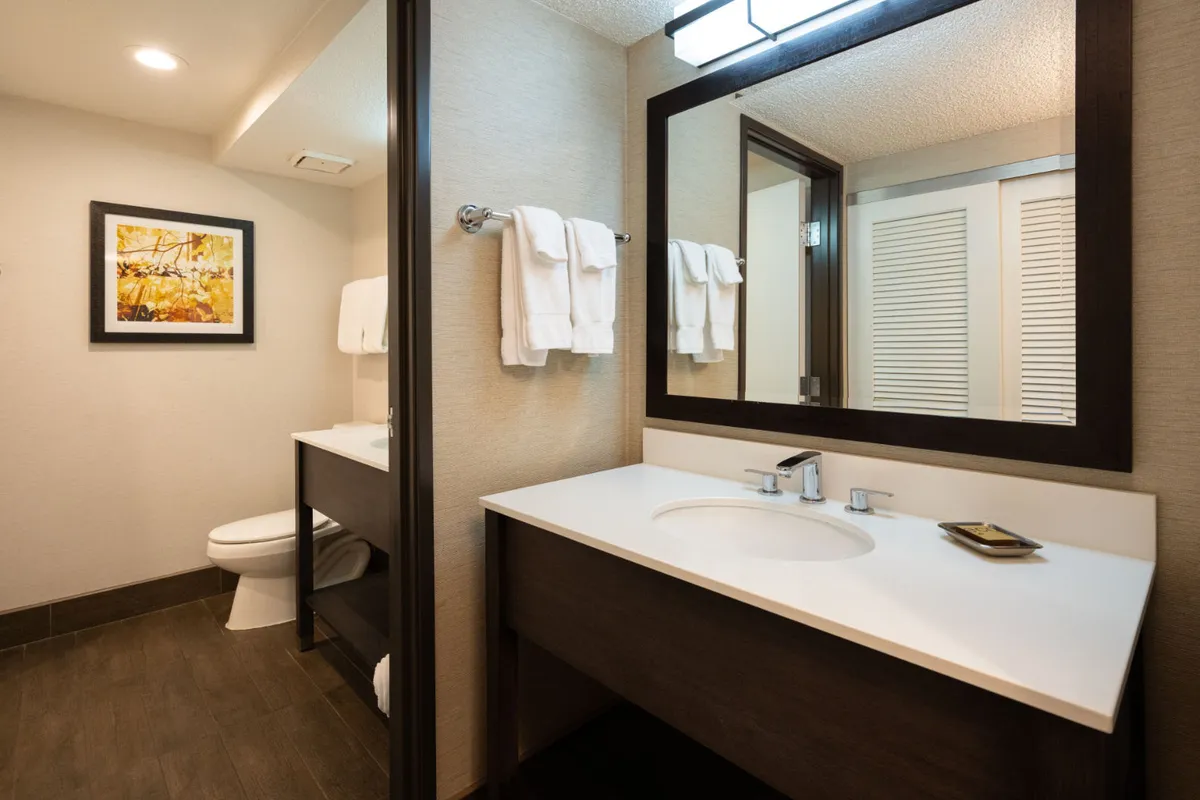 A well-lit bathroom area with a modern sink, large mirror, plenty of fresh towels, and stylish framed artwork. The ambiance is inviting and spa-like, ideal for morning routines or unwinding after a busy day.